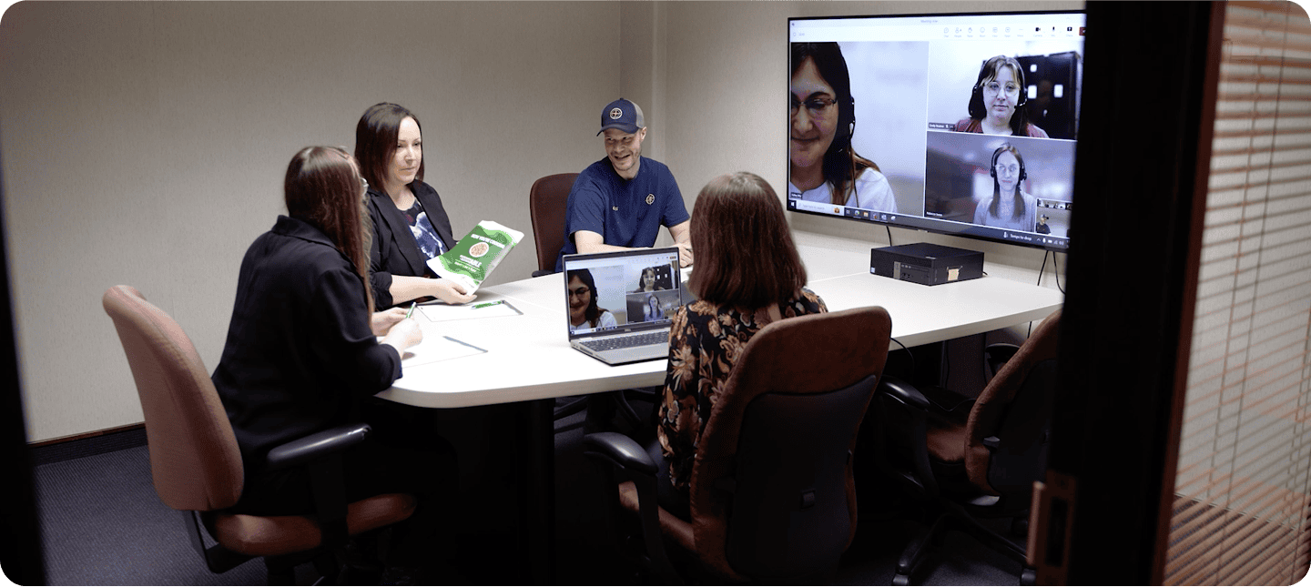 Business team collaborating in a conference room with video call on screen.